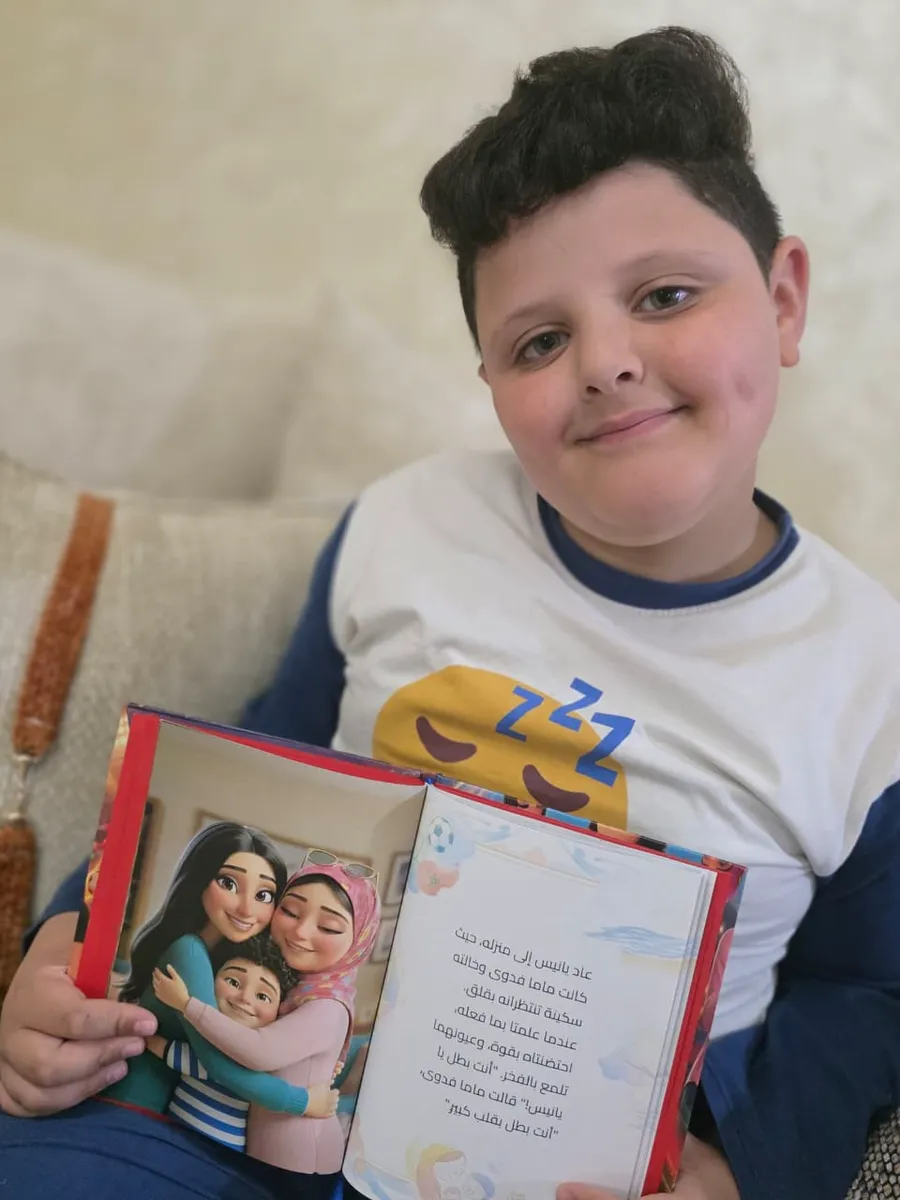 Le même enfant, souriant, montrant une page intérieure de son livre en arabe